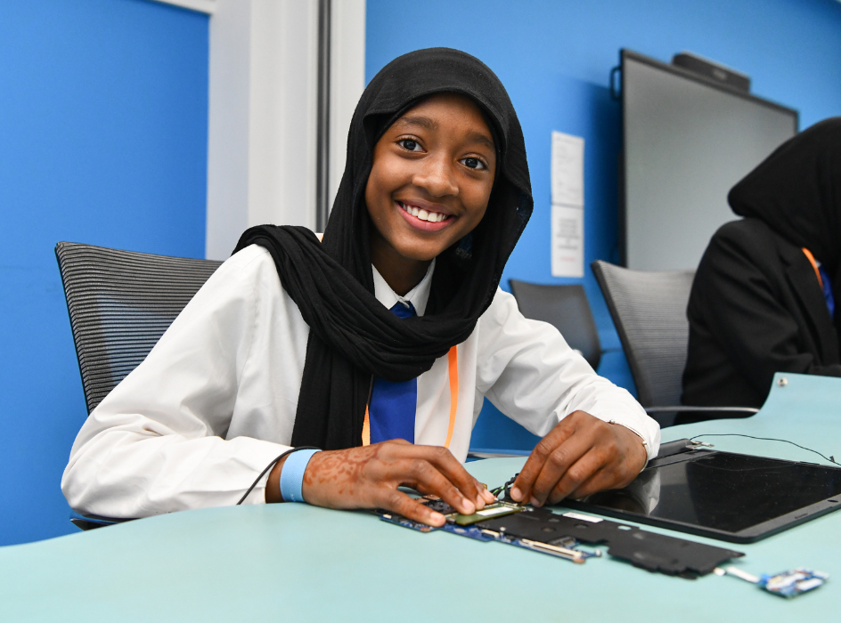 A student wearing a headscarf smiles at the camera while taking part in a workshop at Girl Tech West Midlands